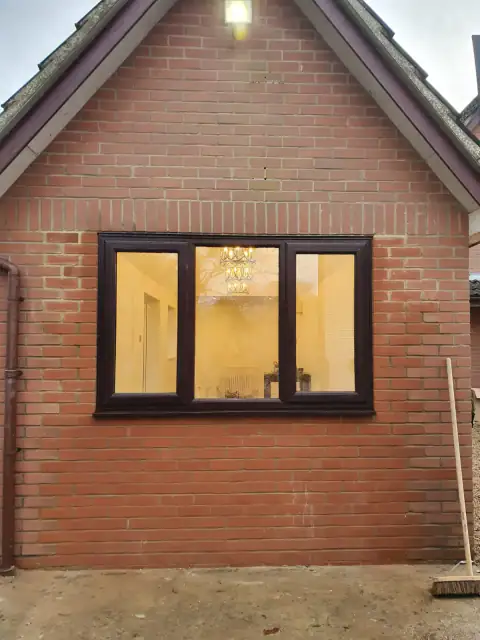 New brickwork and a three-pane window on a B UK Property Services project, lit from inside at dusk